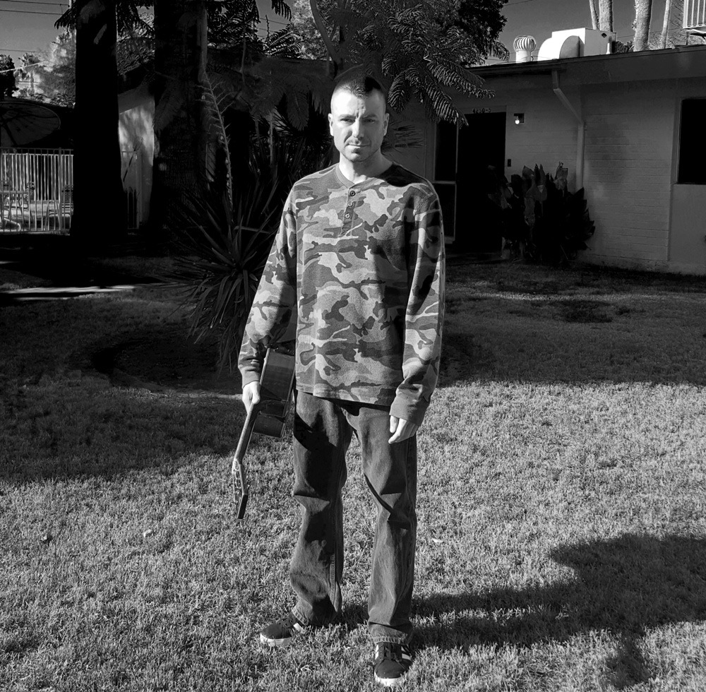 Chance Trahan with an acoustic guitar wearing a camouflage shirt